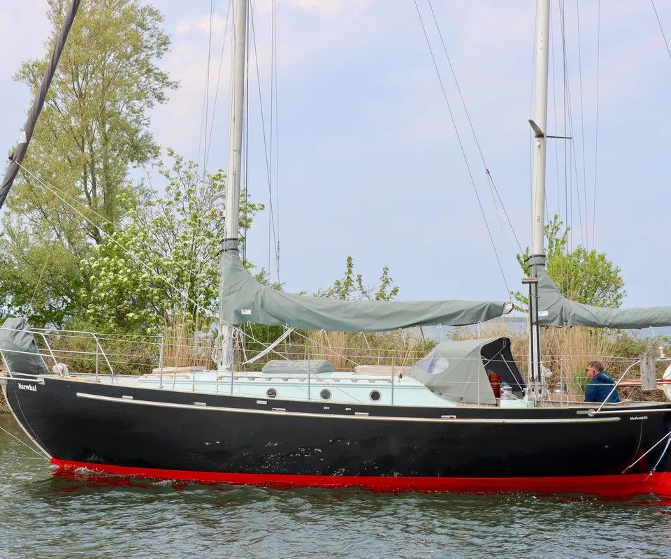 Een zwarte zeilboot met rode onderkant en de naam "Narwhal" op de boeg vaart op het water. — Colin Archer Polar 34