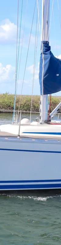 Een witte zeilboot met blauwe strepen vaart op het water, met twee mensen aan boord en een blauw zeil. — Bavaria 38