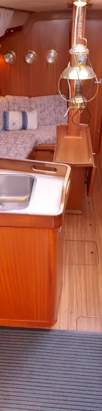 De foto toont het interieur van een boot met een kombuis, zithoek, houten afwerking en een gestreepte vloermat. — Bavaria 38