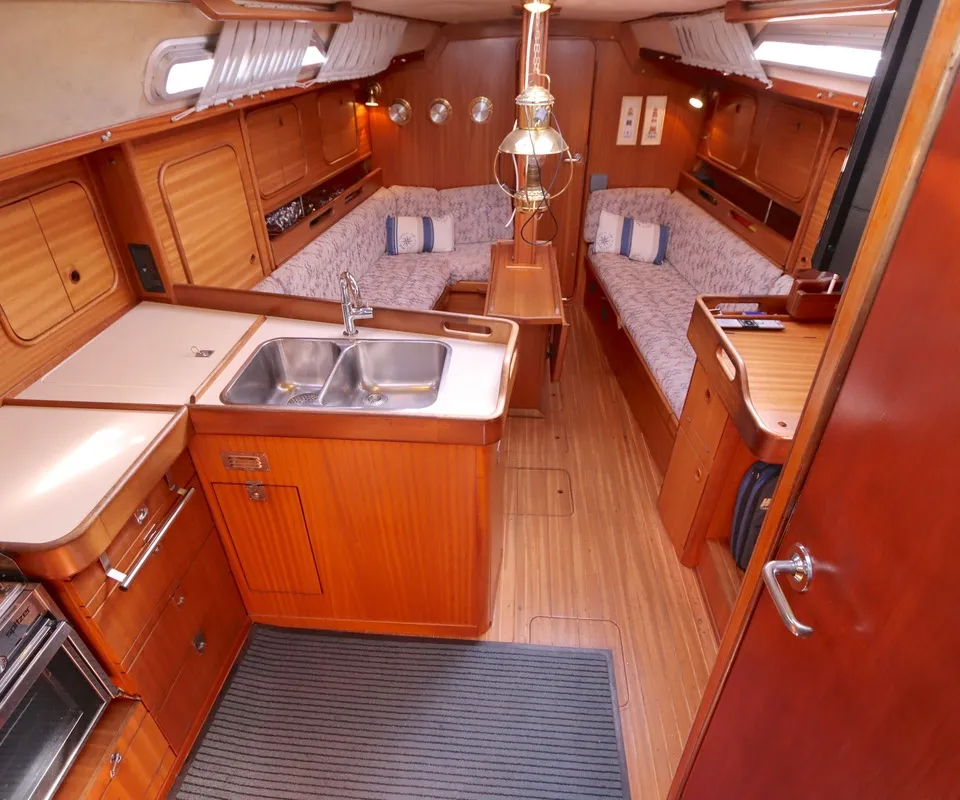 De foto toont het interieur van een boot met een kombuis, zithoek, houten afwerking en een gestreepte vloermat. — Bavaria 38