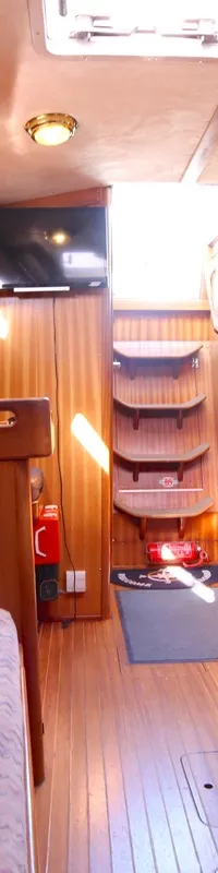 De foto toont het interieur van een boot met houten wanden, een houten vloer en twee banken met gestoffeerde kussens.