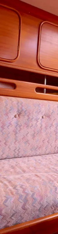 De foto toont een interieur van een boot met een lange bank met patroonbekleding en een kussen met een kompasroos.