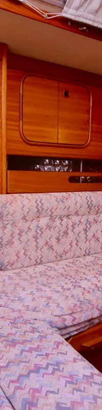 Een houten kajuit met een U-vormige bank met paars-blauwe zigzag bekleding en een wit-blauw kussen. — Bavaria 38