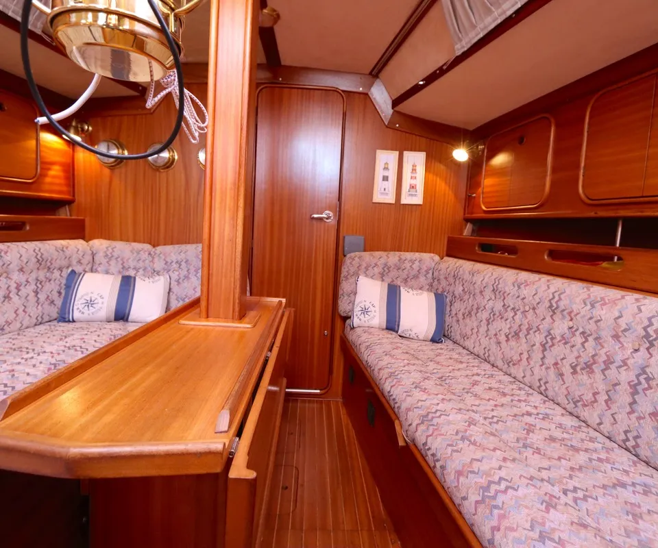 Een interieur van een boot met houten wanden, vloer en meubilair, twee banken met gestoffeerde kussens en een kussen met…