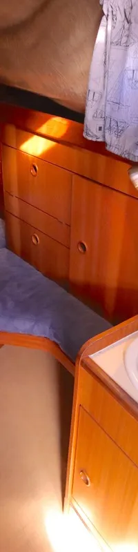 De foto toont een kajuit met een bed, een wastafel, houten kasten en een raam met gordijnen. — Bavaria 38