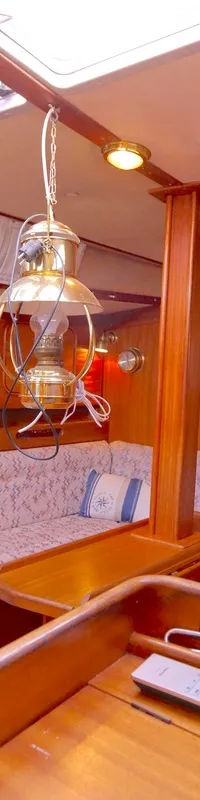 De kajuit van een boot met houten wanden, een bank met stoffen bekleding, een wasbak en een hanglamp. — Bavaria 38