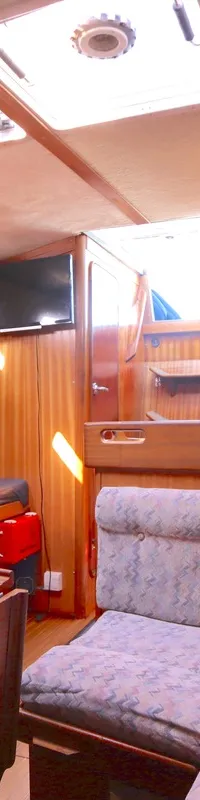 De foto toont het interieur van een boot met houten afwerking, zitbanken met stoffen bekleding en een hangende olielamp.