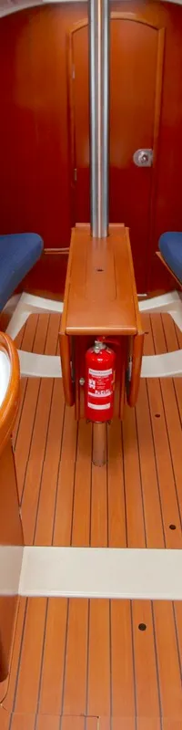 De foto toont het interieur van een boot met een houten vloer, blauwe banken, een aanrecht en een brandblusser.