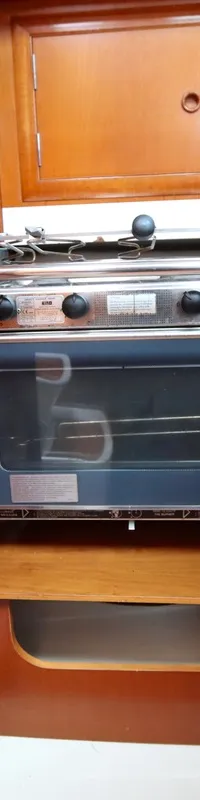 Een ingebouwde oven met twee gaspitten en een houten interieur met kasten en een plank.