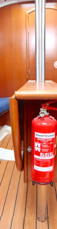 De foto toont het interieur van een boot met twee blauwe banken, een houten vloer en een brandblusser in het midden.