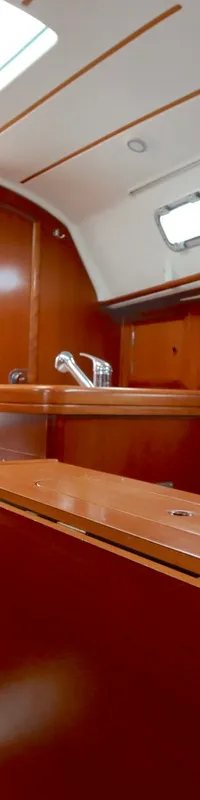 De foto toont het interieur van een boot met houten afwerking, blauwe kussens, een trap en een kombuis met wasbak.