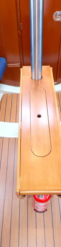 De foto toont een kajuit met twee blauwe banken, een houten vloer, een houten tafel en een brandblusser.