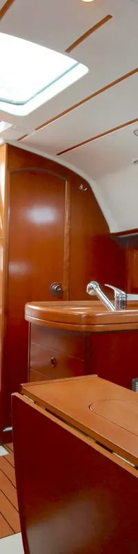 De foto toont het interieur van een boot met houten afwerking, blauwe kussens, een kombuis en een trap naar de kuip.