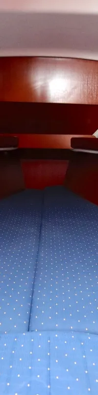 De foto toont een kajuit met een V-vormig bed met blauwe gestippelde kussens en houten zijpanelen.