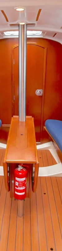 De foto toont het interieur van een kajuit met twee blauwe banken, een houten vloer en een kleine keukenhoek.