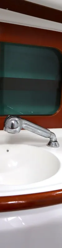 Een witte wastafel met een chromen kraan en zeepdispenser, omringd door wit en donkerbruin houtwerk.