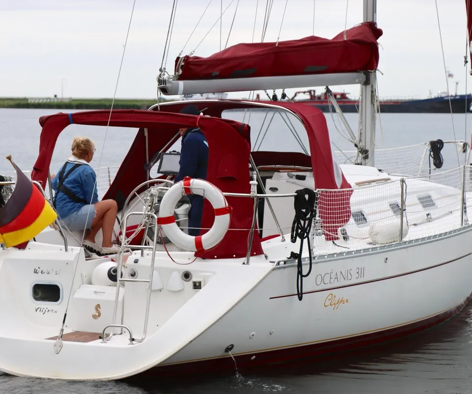 Een witte zeilboot met rode accenten en de naam "OCEANIS 311 Clipper" is te zien op het water. — Beneteau Oceanis 311 Clipper
