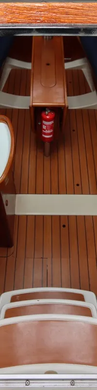Een interieur van een boot met houten vloer en meubilair, een trap, een wasbak en een brandblusser.
