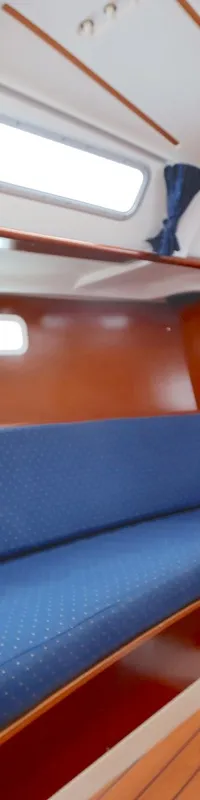 De foto toont het interieur van een boot met een kombuis, blauwe banken, houten panelen en een brandblusser.