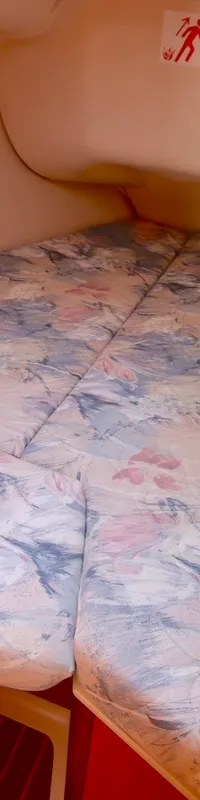 Een kajuit met een V-vormig bed met een bloemenpatroon, een leeslampje en een nooduitgangsymbool. — Hunter 340