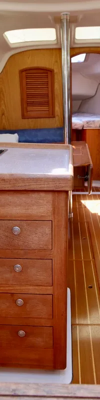 De foto toont het interieur van een boot met een houten afwerking, een kombuis met dubbele spoelbak en blauwe zitbanken.
