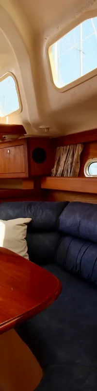 De foto toont het interieur van een boot met een glimmende houten tafel, blauwe banken en ramen. — Hunter 340