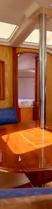 De foto toont het interieur van een boot met een houten tafel, blauwe banken, houten wanden en ramen in het plafond.