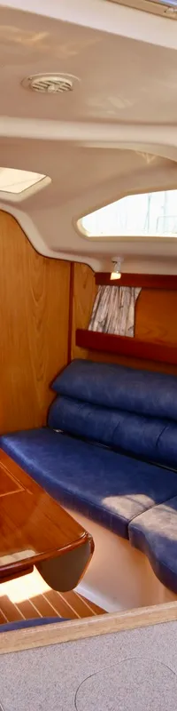 Een interieur van een boot met houten wanden, blauwe banken, een houten tafel en een bed in de achtergrond. — Hunter 340
