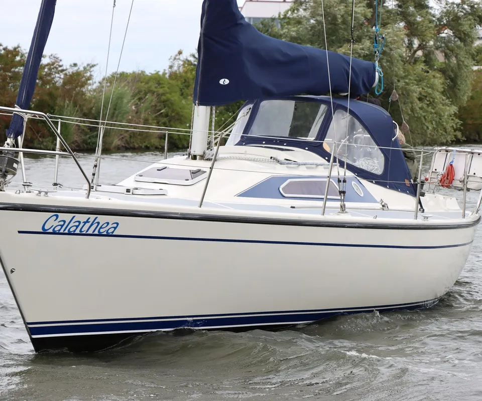 Een witte zeilboot met de naam "Calathea" in blauwe letters op de boeg, vaart op water met lichte golven.