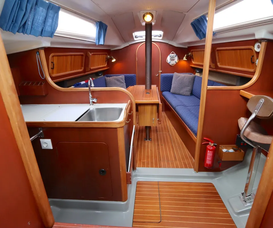 Een interieur van een boot met houten vloer, blauwe banken, een keukenblok met spoelbak en een tafel. — Dehler 34 Optima 106