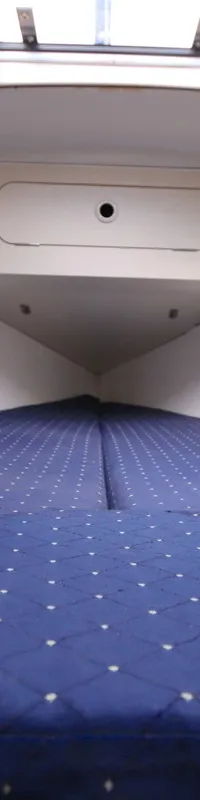 De foto toont een kajuit met een blauw matras met witte stippen, opbergvakken en een dakraam. — Dehler 34 Optima 106
