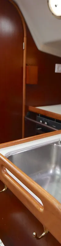 Een interieur van een boot met een rvs-gootsteen, een kraan, een fornuis en houten kasten en panelen. — Dehler 34 Optima 106