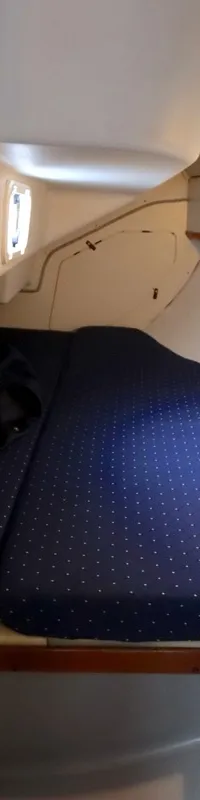 De foto toont een kajuit met een groot blauw gestippeld bed en een kleiner bijpassend zitkussen. — Dehler 34 Optima 106
