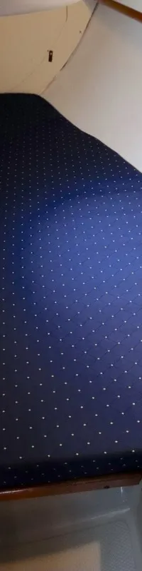 Een kajuit met een donkerblauw gestippeld matras, witte wanden en houten accenten. — Dehler 34 Optima 106