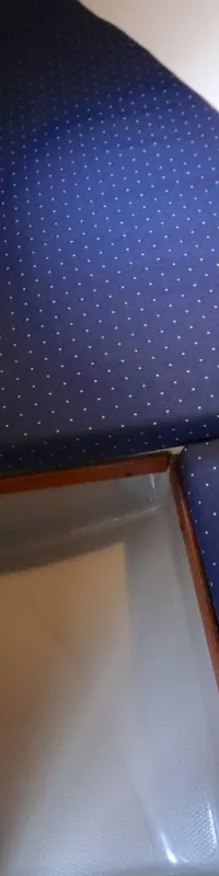 De foto toont een interieur van een boot met blauwe gestippelde kussens, witte wanden en een houten kastje.