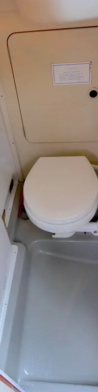 De foto toont een compacte, witte badkamer met een wastafel, toilet, en een grijze douchebak.