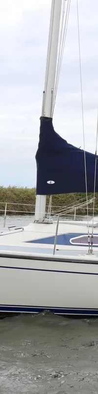 Een witte zeilboot met blauwe accenten en de naam "Calathea" vaart op water, met twee personen aan boord.