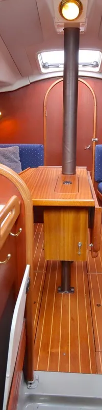 De foto toont het interieur van een boot met een kombuis aan de linkerkant en twee banken met een tafel in het midden.