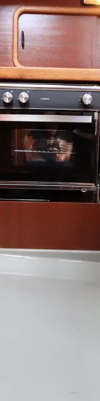 Een ingebouwde oven met vier draaiknoppen en een glazen deur is zichtbaar in een houten interieur.