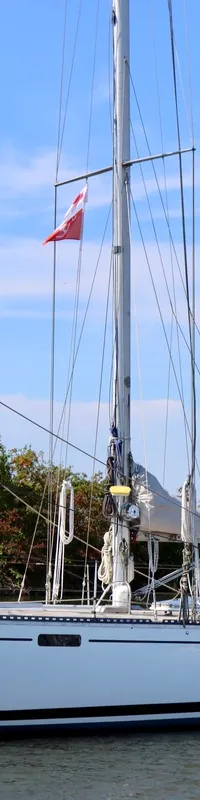 Een witte zeilboot met twee masten en opgerolde zeilen ligt in het water onder een blauwe hemel. — RJ 140