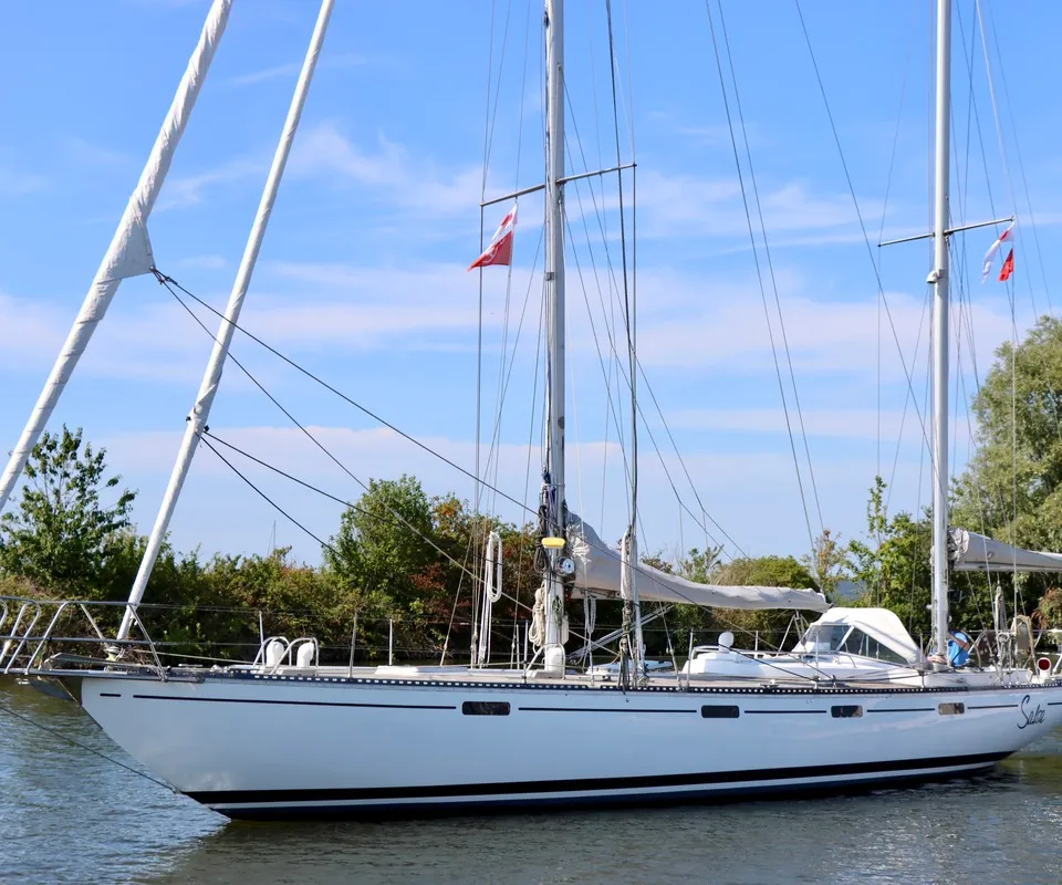 Een witte zeilboot met twee masten en opgerolde zeilen ligt in het water onder een blauwe hemel. — RJ 140