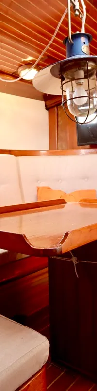 De foto toont het interieur van een boot met houten wanden en plafond, een zithoek met lichte kussens en een houten tafel.