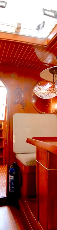 De foto toont het interieur van een boot met houten wanden en plafond, witte kussens en een houten tafel. — RJ 140
