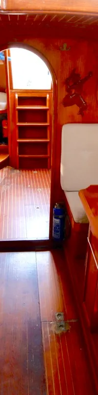 De foto toont het interieur van een boot met houten wanden en vloer, witte banken en een houten tafel. — RJ 140