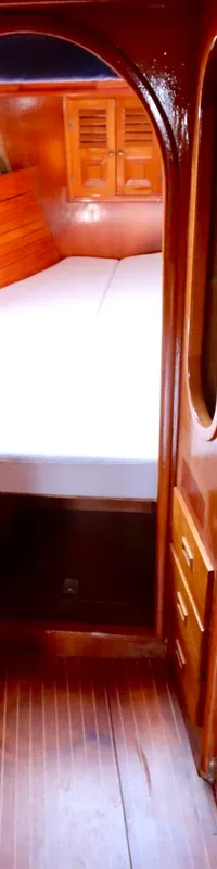 Een houten kajuitinterieur met een doorgang naar een slaapgedeelte met een wit matras.