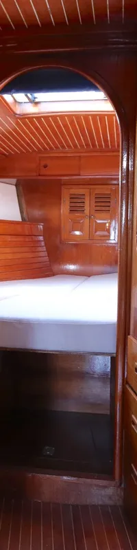 Een houten gangpad met aan weerszijden houten deuren en kasten, leidend naar een kajuit met een tweepersoonsbed. — RJ 140