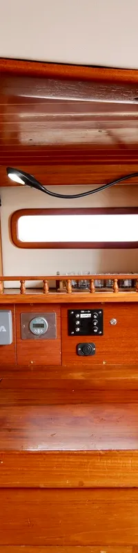 Een houten interieur van een boot met een werkblad, diverse meters, schakelaars en een klein raam. — RJ 140