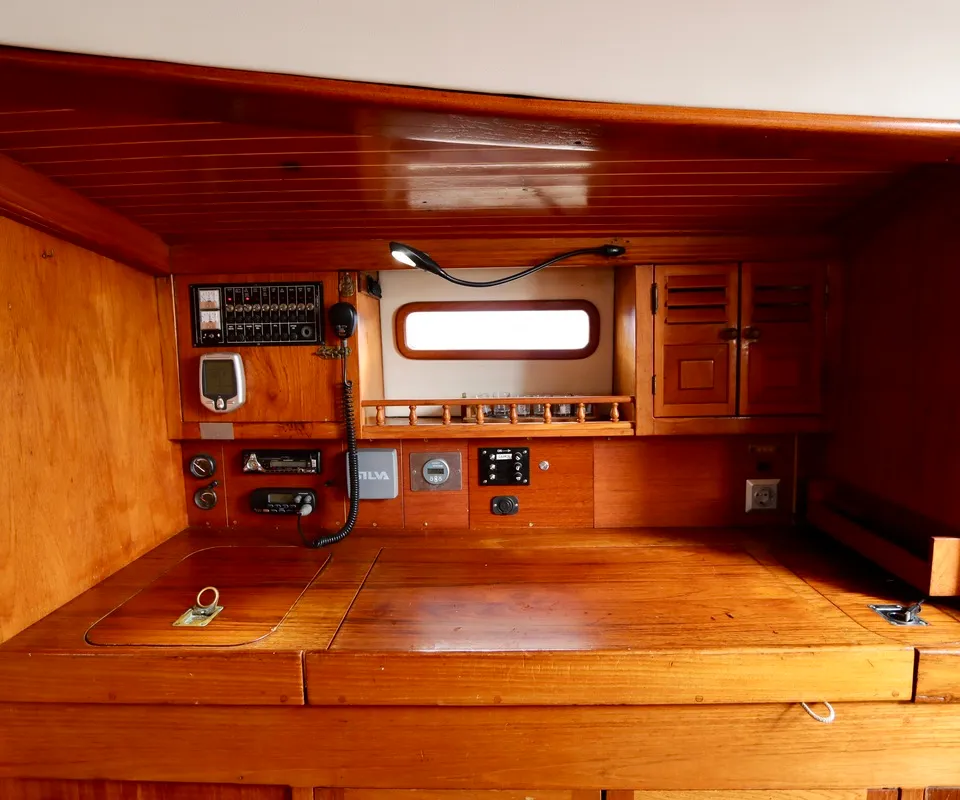 Een houten interieur van een boot met een werkblad, diverse meters, schakelaars en een klein raam. — RJ 140