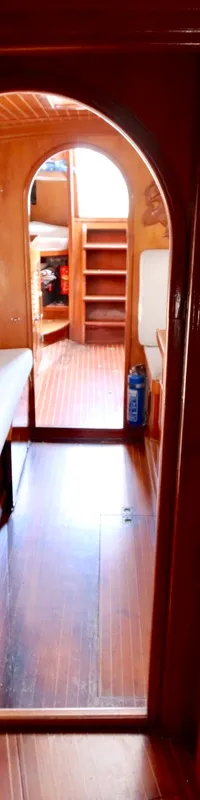 Een houten interieur van een boot met een gang, zitbanken, een deur en een brandblusser. — RJ 140