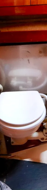 Een scheepstoilet met een handpomp en houten lambrisering in een kleine ruimte.